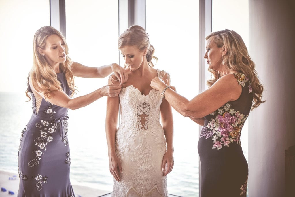 The bride's family assists her at the ocean front suite at Eden Roc hotel in Miami Beach in her Eve of Milady wedding dress with beaded sleeves and long lace train