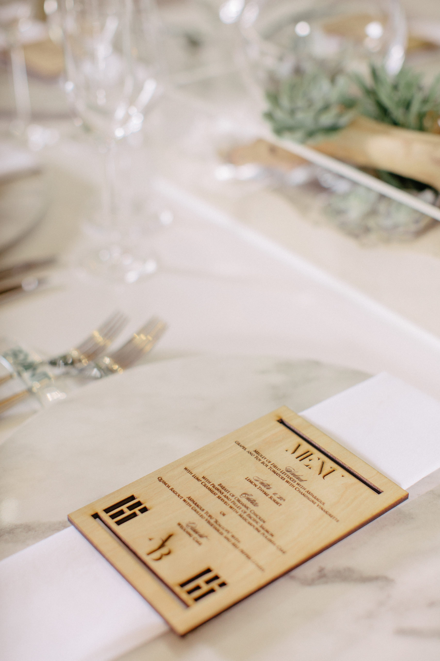 Acrylic wedding table with white wood dowel chairs and statement chairs at either end, featuring marble charger plates and resin name plates that served as unique place cards with a wood engraved menu buckle | Laser cut wood engraved menus