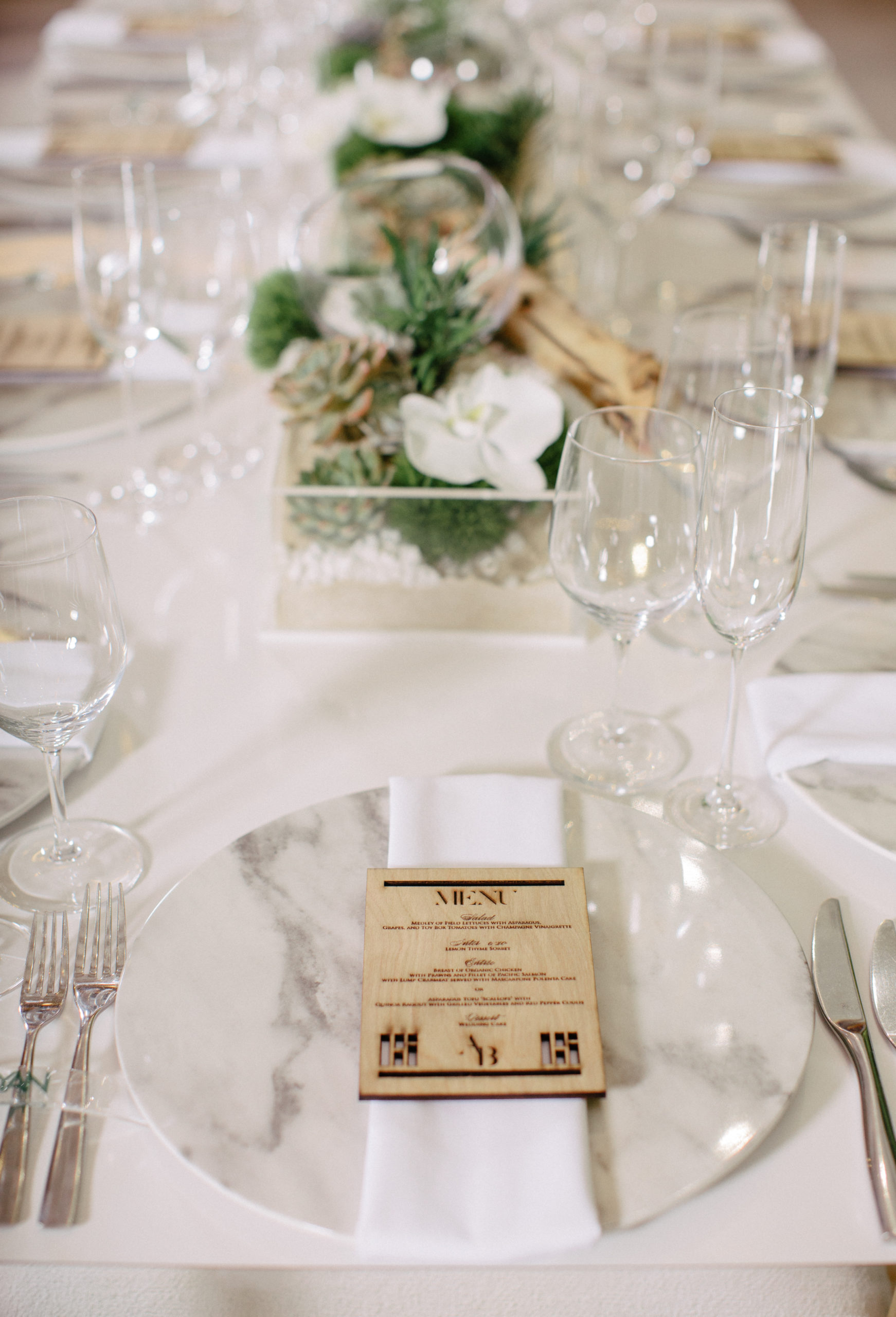 Acrylic wedding table with white wood dowel chairs and statement chairs at either end, featuring marble charger plates and resin name plates that served as unique place cards with a wood engraved menu buckle