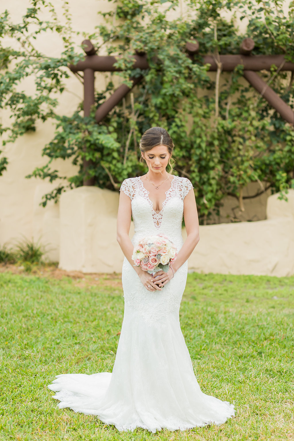 The bride's wedding dress is lace, open back, with beaded spine, lace detailing, lace cap sleeves and a low cut front. She carries a simple rose cluster bouquet with dusty miller