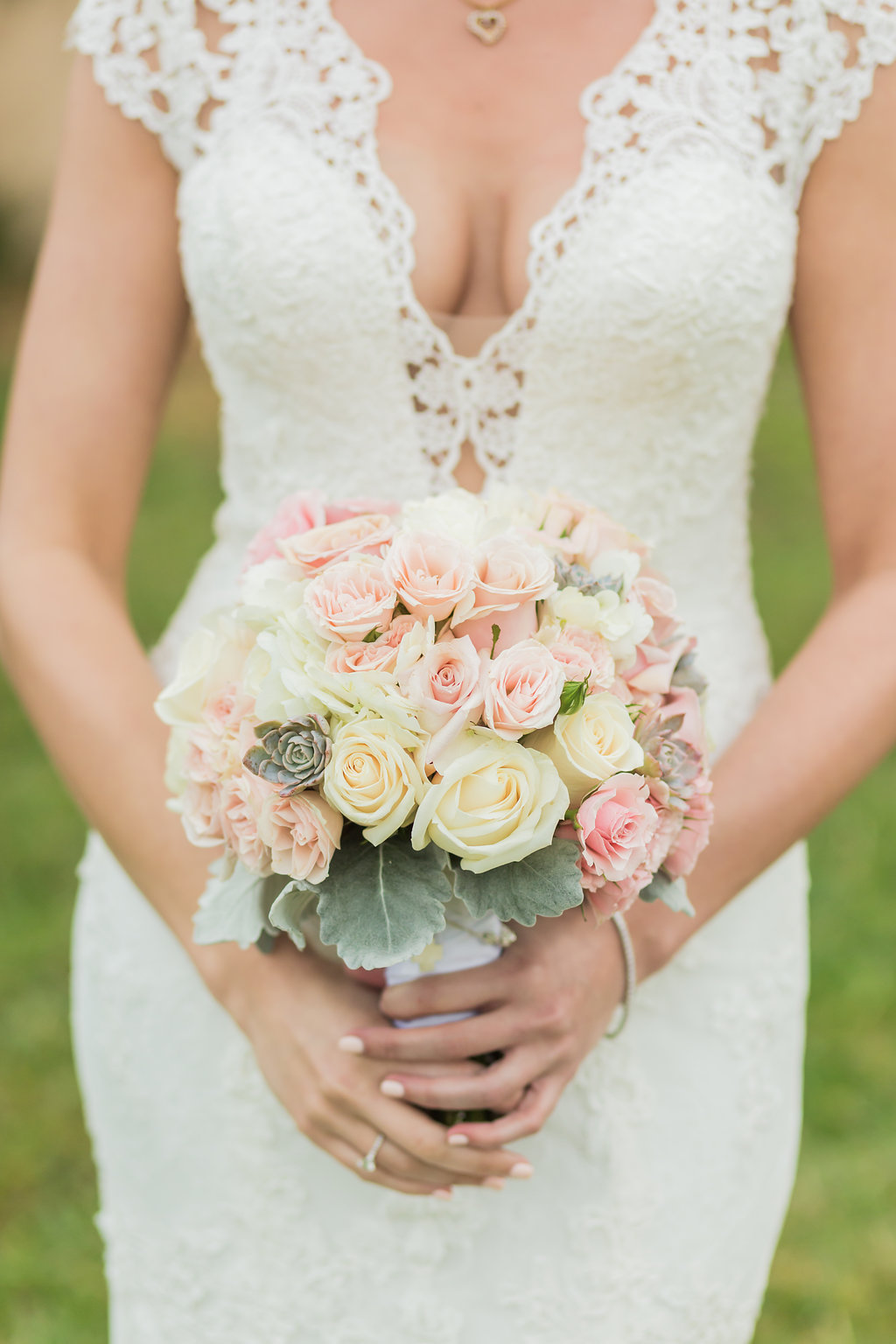 The bride's wedding dress is lace, open back, with beaded spine, lace detailing, lace cap sleeves and a low cut front. She carries a simple rose cluster bouquet with dusty miller