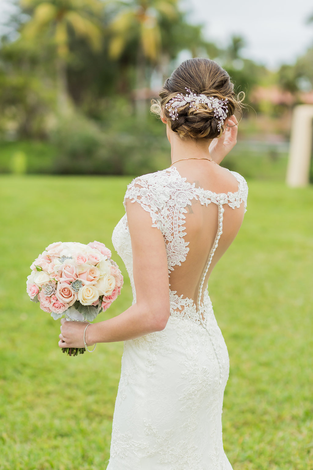The bride's wedding dress is lace, open back, with beaded spine, lace detailing, lace cap sleeves and a low cut front with rose bouquet and dusty miller