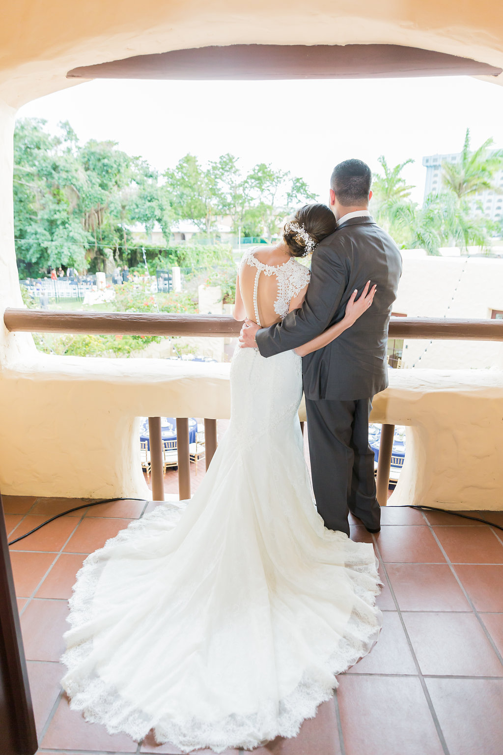 The bride and groom looked over their guests from the Curtiss Mansion balcony in her lace open back, beaded and lace wedding dress with low undo and hair piece