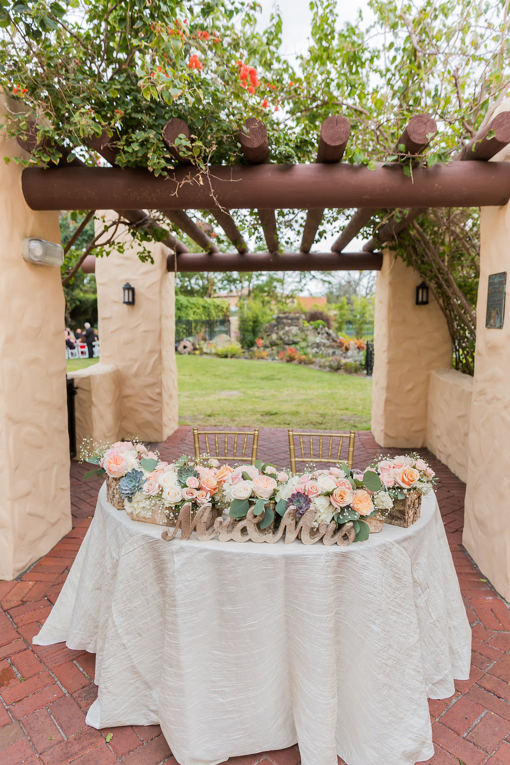 The Curtiss Mansion wedding sweetheart table sat under the wooden canopy. It has a gold Mr. and Mrs. sign and garden centerpiece with ivory fortuny linen