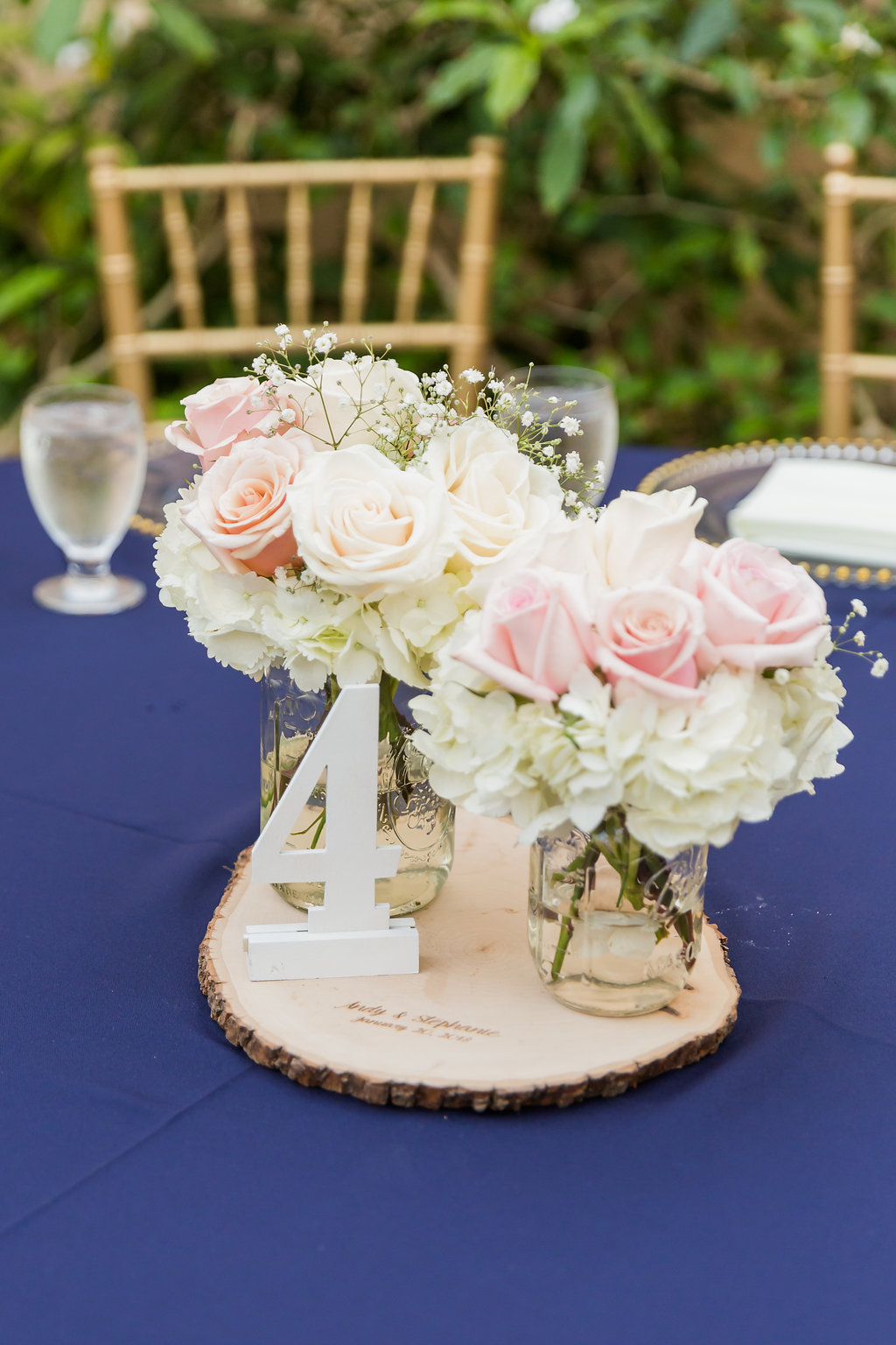 The Curtiss Mansion wedding had dinner in the courtyard with navy blue linens, gold beaded charger plates, gold chiavari chairs, and ivory seat cushions. The centerpieces were simple wood slabs, engraved with the couple's wedding details, a white wooden table number and mason jar floral vases