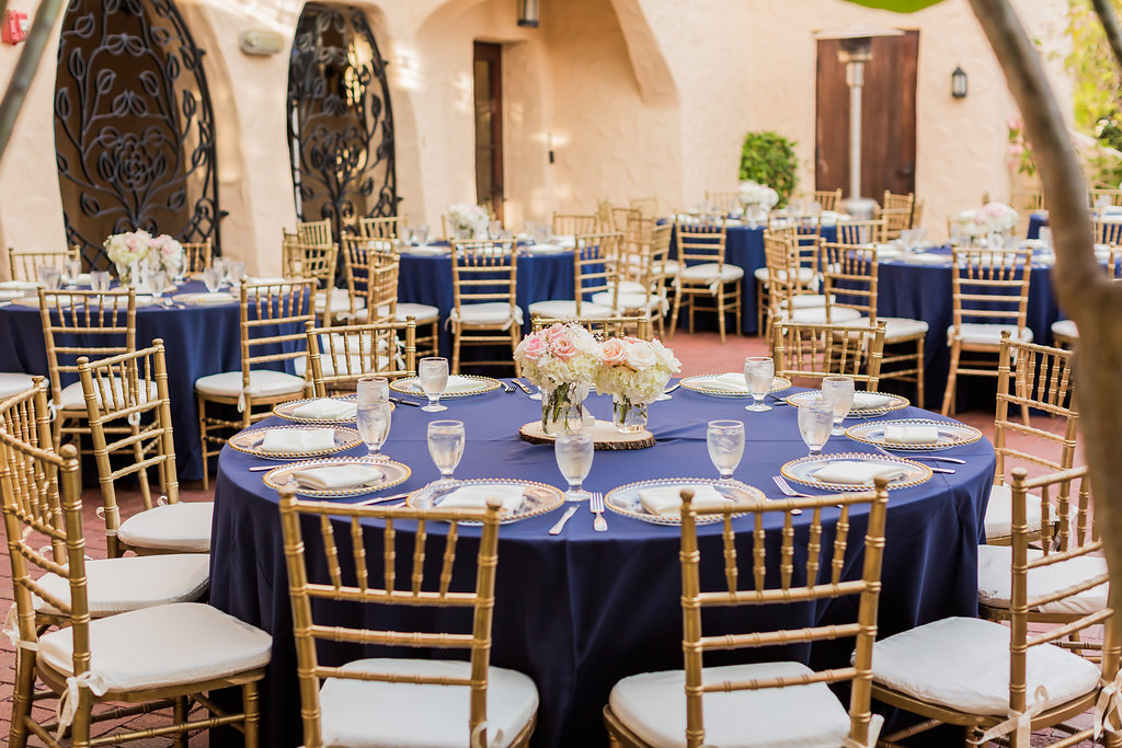 The Curtiss Mansion wedding had dinner in the courtyard with navy blue linens, gold beaded charger plates, gold chiavari chairs, and ivory seat cushions