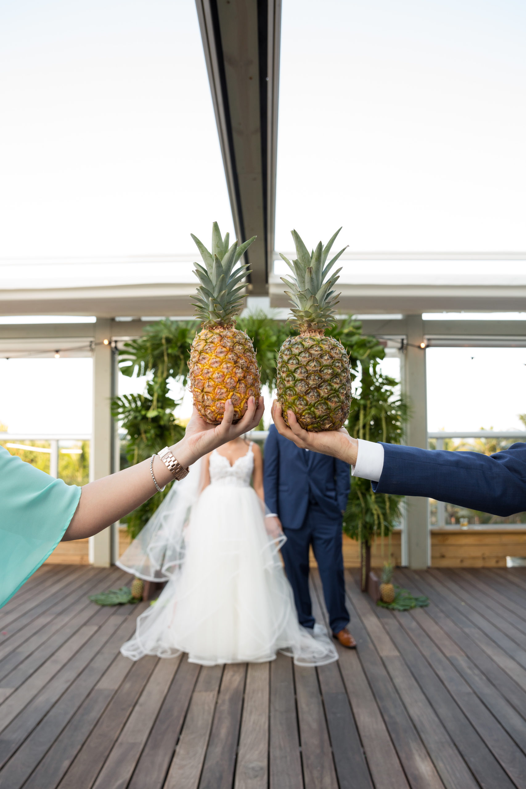 For this pineapple wedding at the Confidante miami beach, the bride and groom's faces are hidden behind the maid of honor and best man holding a pineapple