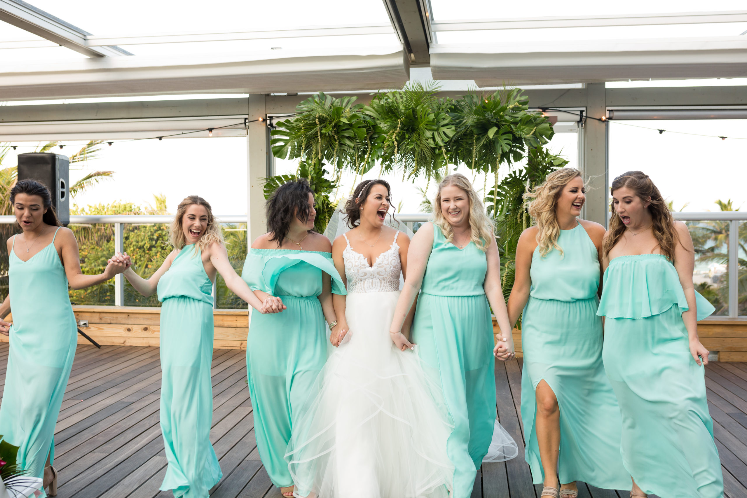 The bride and her bridesmaids walking holding hands in seafoam mint bridesmaids dresses