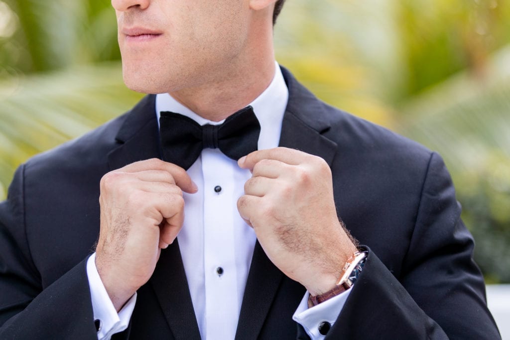 groom straightens his black bow tie