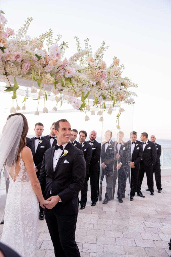 groomsmen line up behind the acrylic structure at a wedding ceremony