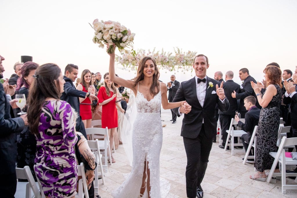 bride and groom celebrate by smiling and raising their arms after they walk back down the aisle as husband and wife
