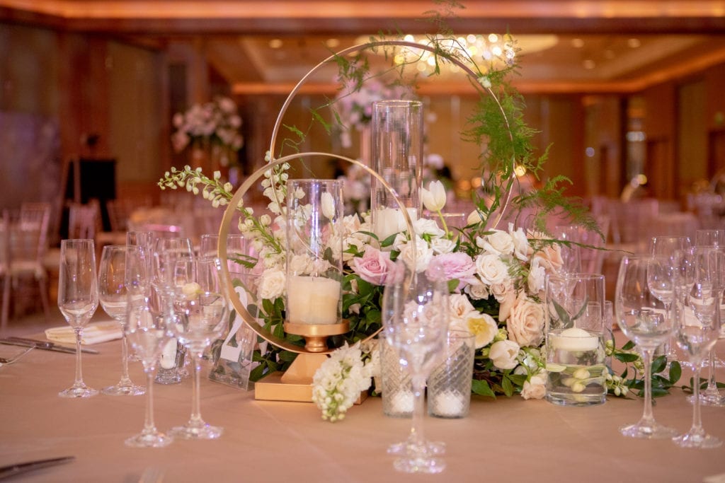 two gold hoops of different heights houses a pillar candle and loose blush and ivory flowers with greenery