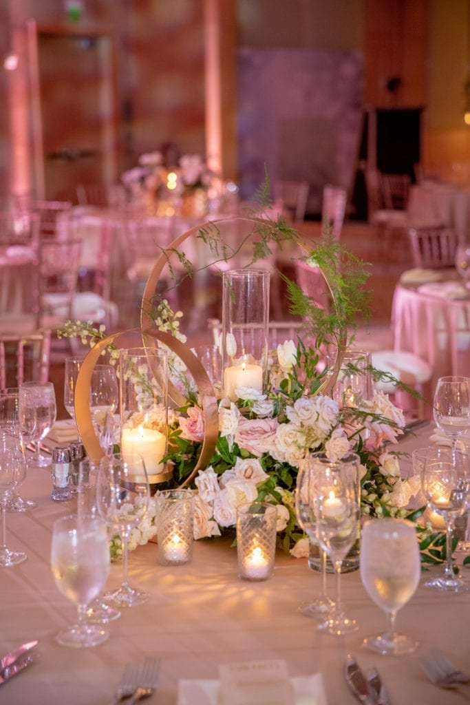 wedding centerpiece with two gold hoops of altering heights and filled with greenery and blush and white flowers