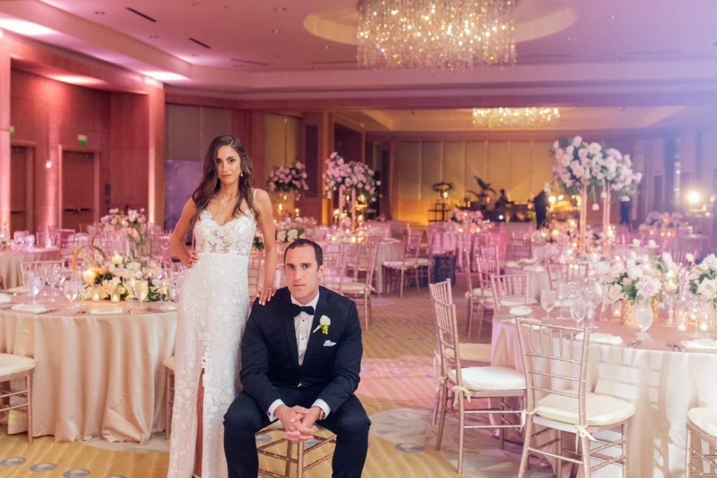 bride and groom pose in front of their guest tables with champagne satin linen and champagne chiavari chairs at Ritz Carlton Ft. Lauderdale