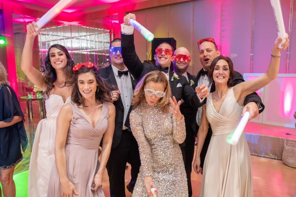 wedding guests enjoy the party props for Hora Loca at Ritz Carlton Ft. Lauderdale wearing sunglasses and carrying foam glow sticks