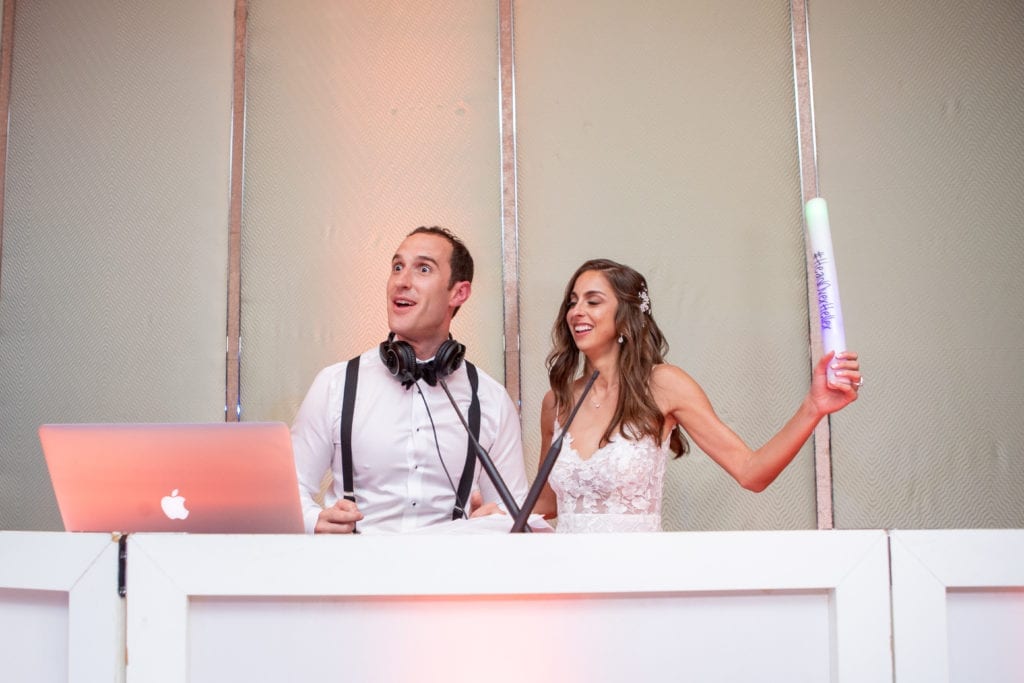bride and groom hop on stage with props and headphones to take the place of the DJ during their wedding