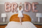 the bride stand on her bed with BRIDE balloons behind her