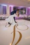 groom dips his bride on their white vinyl dance floor with gold monogram