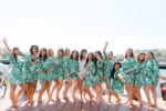 14 bridesmaids wear palm leaf robes while having fun posing on the boat dock