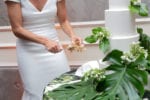 A white cake with tropical leaves is cut by the bride revealing a delicious carrot cake center