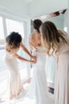 the bridesmaids help the bride zip into her wedding gown