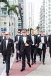 groom and groomsman walk in downtown Miami wearing sunglasses and sipping on their drinks