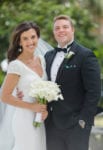 bride and groom smile as she holder her orchid bouquet