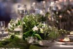 the tropical centerpiece is filled with green palm leaves and accents of white flowers with floating candles
