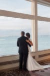 bride and groom stare out the large window of the Rusty Pelican ballroom