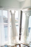 the v-neck cap sleeved wedding gown hangs in front of a window next to a floor mirror