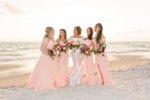 the bridesmaids wear varying styles of blush long dresses and hold pink and peach bouquets