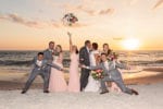 the wedding party celebrates as the bride and groom kiss in front of the sunset in the ocean at La Playa Naples