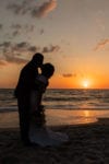 the sun sets behind a silhouetted bride and groom at La Playa Naples