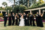 the wedding party wearing all black smiles and cheers as they surround the bride and groom