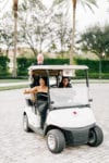 the mother of the bride gives a thumbs up as she rides in the golfcart driven by Oh My Occasions and the father of the bride hangs off the back