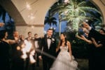 bride and groom smile under a tunnel of sparklers that their wedding party holds high