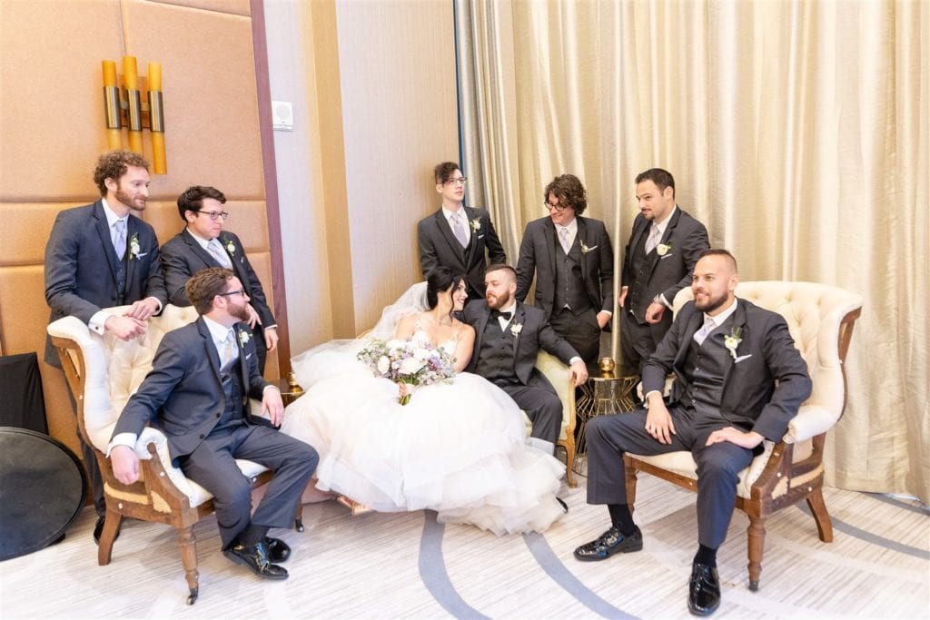 The bride and groom with their groomsmen sitting all together on a couch at The Conrad Fort Lauderdale Beach, wedding planned by Oh My Occasions