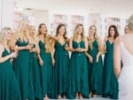 bridesmaids react to seeing the bride wearing green emerald bridesmaids dresses and holding champagne