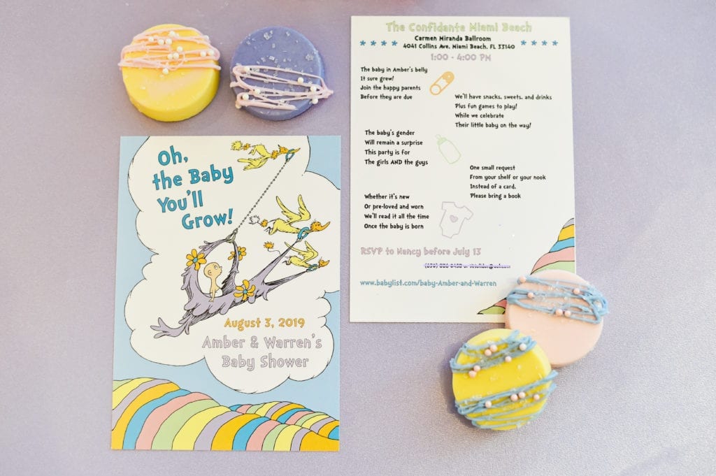 Dr. Seuss themed baby shower Oh The Places You’ll Go baby shower invitation with rhyming lyrics designed by Oh My Occasions next to pastel cookie