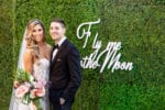 bride and groom next to wood sign on hedge wall