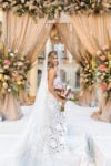 bride and groom underneath blush draped chuppah with pampas grass and roses with white stage and berta wedding gown