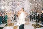 confetti fills the air on the gold and white checkerboard dance floor as hora loca performers dance and the bride and groom laugh at JW Marriott Marquis Miami wedding