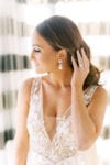 bride fixes her curls with large pear earring and v-cut wedding gown from chic parisien