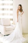 bride playfully touches her curled hair as she admires her chic parisien wedding gown with champagne bow belt