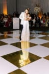 bride and groom dance on their gold and white checkerboard dance floor wrap by oh my occasions