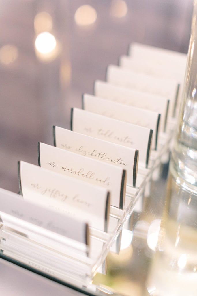 White name cards placed on a mirror table cover in a line at The Mandarin Oriental, wedding planned by Oh My Occasions
