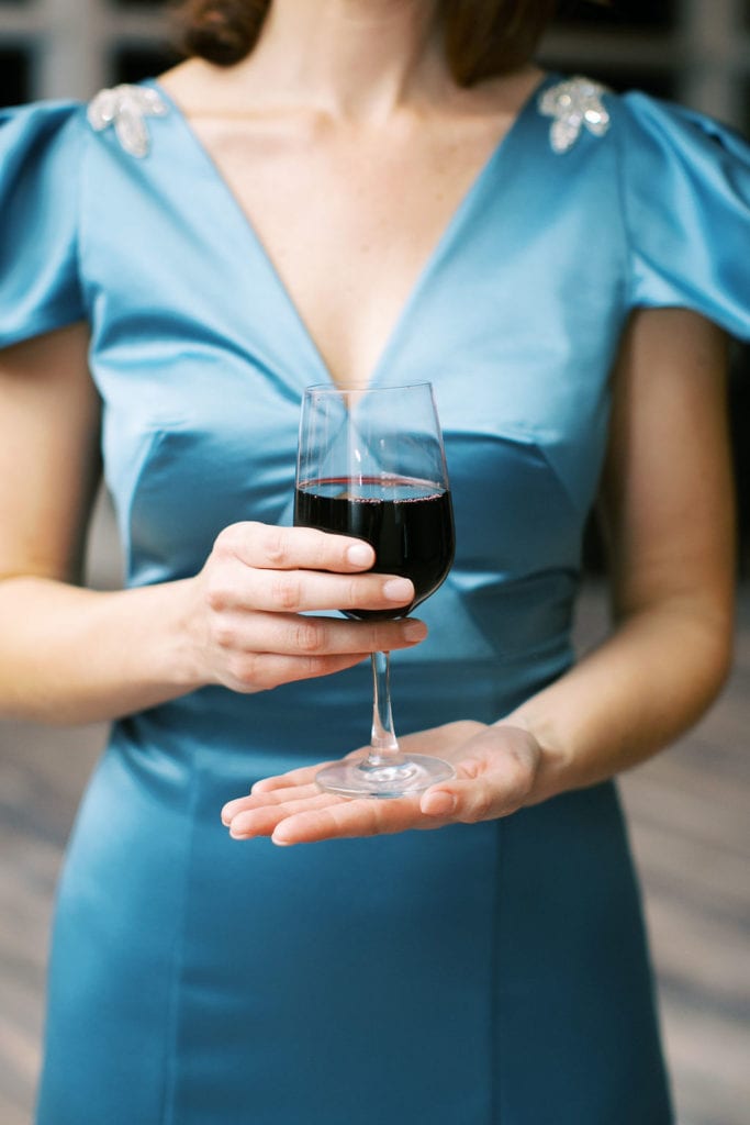 A guest holding a glass of red wine and wearing a blue teal v-cut dress at The Mandarin Oriental, wedding planned by Oh My Occasions