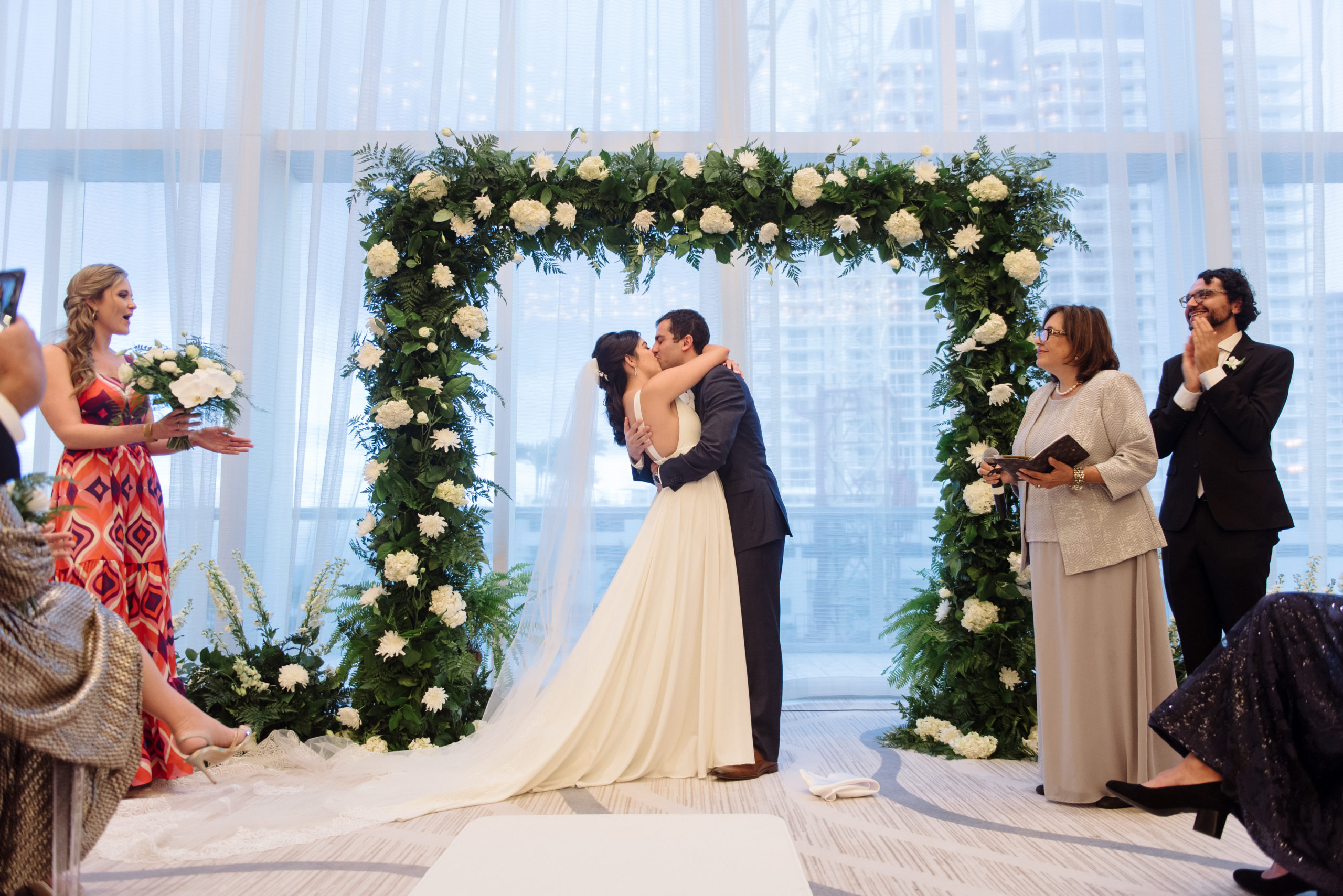 The bride and groom kissing at the alter under a gorgeous arch of white flowers at the Conrad Fort Lauderdale Beach, wedding planned by Oh My Occasions