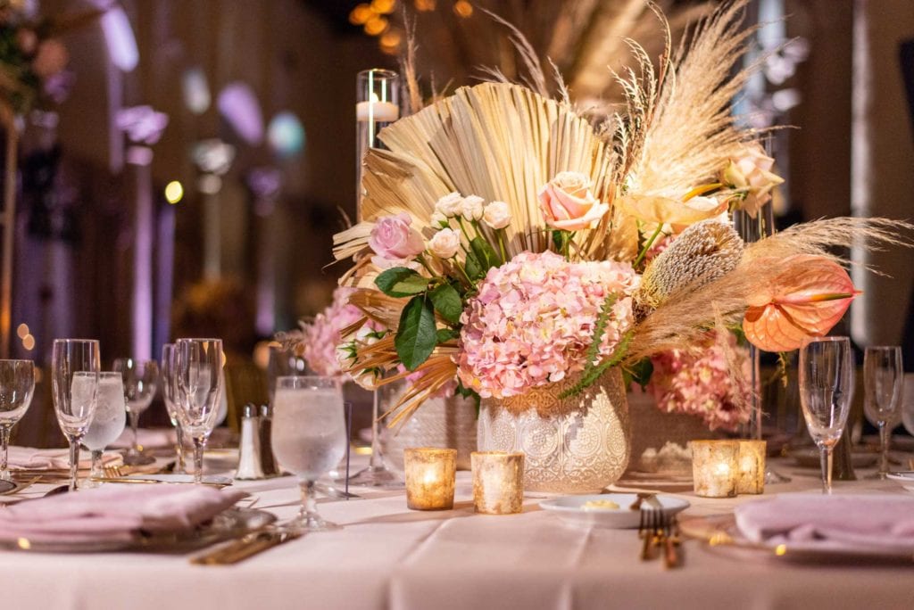 Pink floral centerpiece inside white vase on table.
