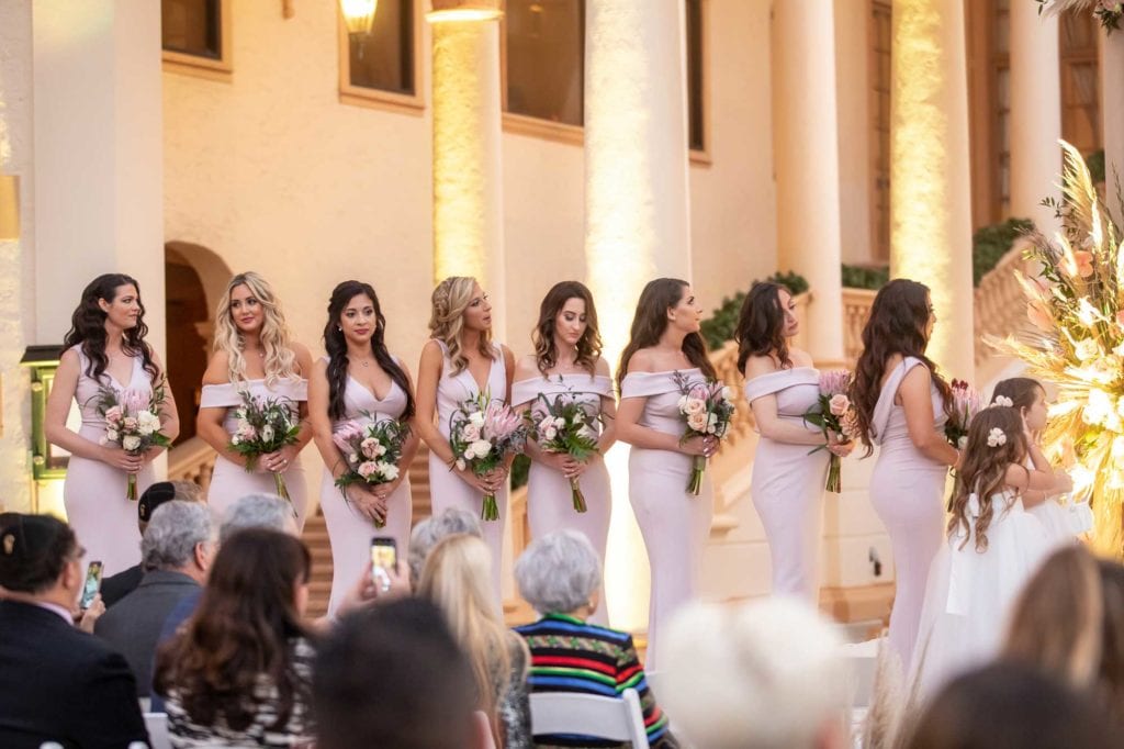 Bridesmaids wearing blush gowns stand next to the bride with their matching bouquets during the ceremony at The Baltimore Hotel in Miami Coral Gables, wedding planned by Oh My Occasions
